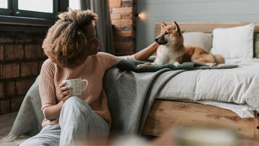 woman sitting on the floor petting a dog laying on the bed